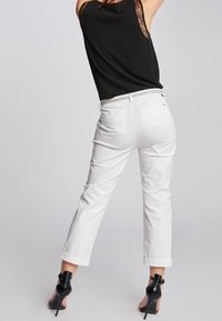 Pantaloni bianchi accorciati con risvolti, tessuto strutturato. Abbinati a un top senza maniche nero con dettagli in pizzo e scarpe con tacchi alti.