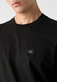 Black short-sleeve cotton t-shirt with a crew neckline and small, rectangular Calvin Klein Jeans logo patch on the left side.