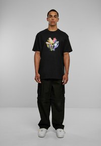 Sort bomulds t-shirt med farverigt grafisk design i midten, parret med løstsiddende sorte cargo bukser og hvide sneakers.