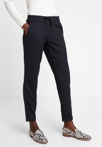 Zwarte slim-fit broek met een elastische tailleband en trekkoord. Soepele stof, zijzakken en enkellange boorden. Gecombineerd met gestreepte schoenen.