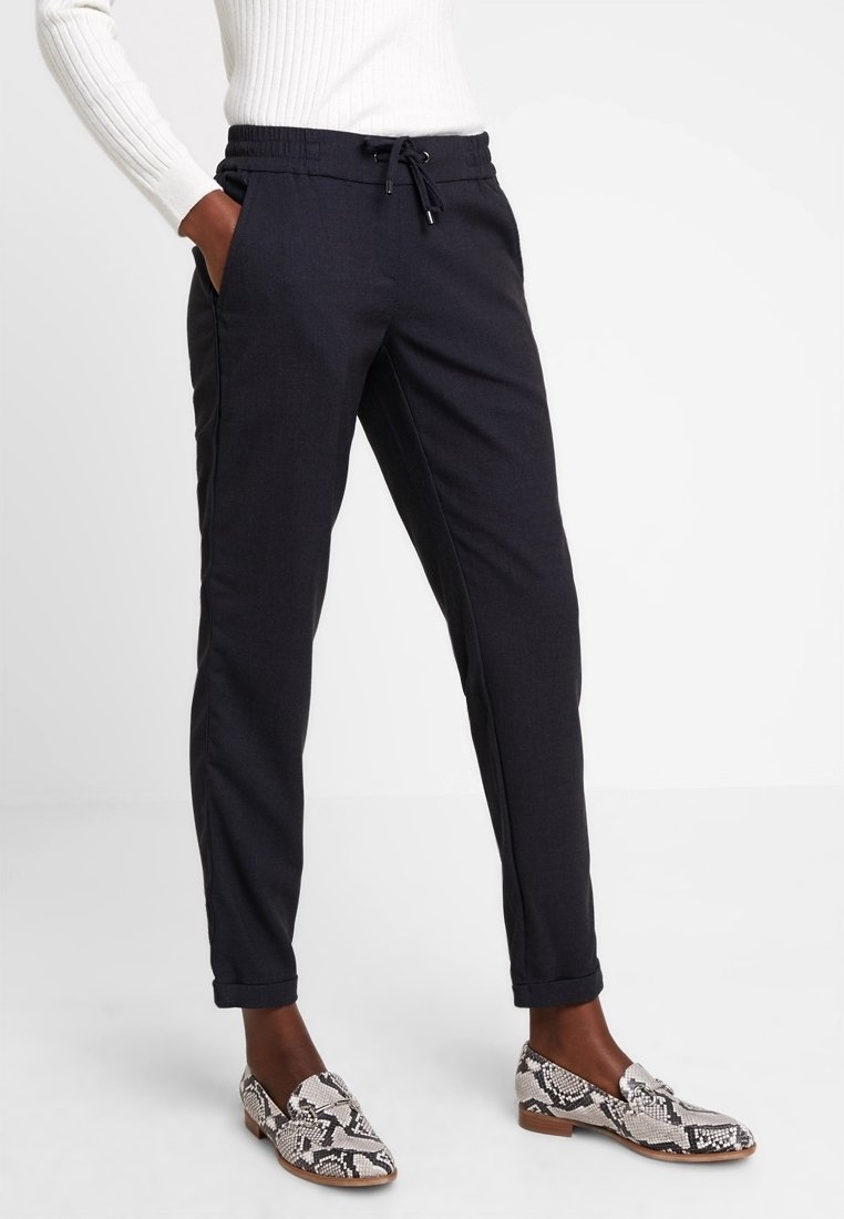 Zwarte slim-fit broek met een elastische tailleband en trekkoord. Soepele stof, zijzakken en enkellange boorden. Gecombineerd met gestreepte schoenen.