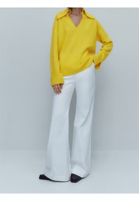 Geel gebreid sweater met een V-hals en een oversized kraag, gecombineerd met witte flared broek en zwarte schoenen. Glad textuur en ontspannen pasvorm.