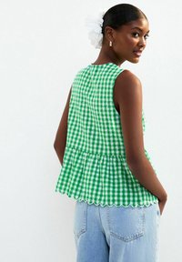Grön och vit rutigt ärmlös topp med peplumslut, vågiga kanter och subtil textur. Bärs med ljusblå högmidjade jeans.