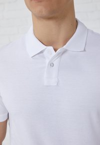 Witte polo shirt met een gestructureerde stof, klassieke kraag, twee-knopen sluiting en korte mouwen. Eenvoudig en strakke ontwerp.