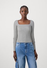 Haut à manches longues gris côtelé avec un décollet�é carré, associé à un jean cargo bleu clair avec poches latérales et une coupe décontractée.