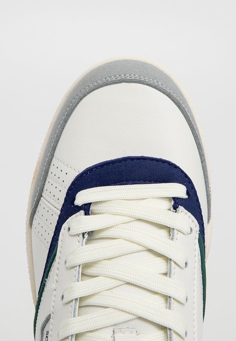 Weiße Leder-Sneaker mit marineblauen und grünen Akzenten, grauem Wildleder-Überzug an der Zehenkappe, strukturiertem Obermaterial und weißem Schnürverschluss.