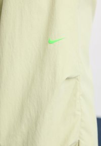 Lichtgele Nike-jack met een gladde, lichtgewicht stof en een opvallend neon groene logo aan de linkerkant.