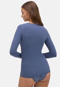 Top de manga larga ajustado en algodón azul tenue con escote redondo, combinado con ropa interior azul con adornos de encaje y un patrón floral.