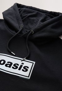 Zwarte hoodie met een capuchon met trekkoord, een gestructureerde stof en een witte "oasis"-logo binnen een rechthoekige rand. Inclusief zilverkleurige metalen accenten.