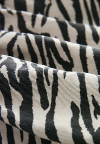 Gros plan d’un tissu rayé zèbre noir et blanc avec une texture visible et des plis créant un motif ondulé.