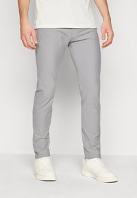 Pantaloni slim-fit grigi realizzati in tessuto leggero, con una texture liscia, gambe affusolate e tasche laterali, abbinati a sneakers bianche.