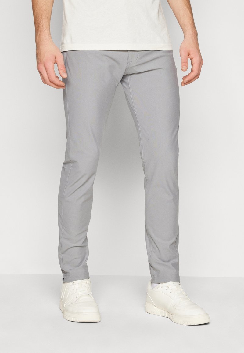 Pantaloni slim-fit grigi realizzati in tessuto leggero, con una texture liscia, gambe affusolate e tasche laterali, abbinati a sneakers bianche.