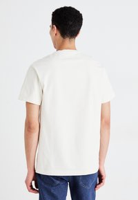 Lichtbeige katoenen T-shirt met korte mouwen en een ronde hals, met een gladde textuur en een eenvoudig ontwerp. Zichtbare stiksels aan de zoom.