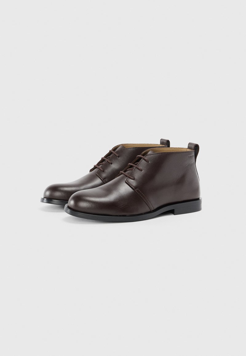 Bottines en cuir marron avec un bout rond, des lacets fins et un petit talon. Présentent une texture lisse et un design minimaliste.