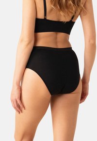 Culottes taille haute en coton noir avec une texture lisse, taille élastique et détails de couture minimaux en haut.