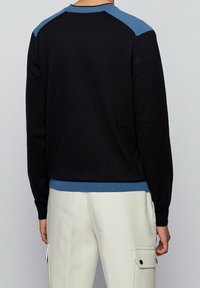 Maglione nero con dettagli blu sulle spalle, scollo a girocollo e polsini a coste. Texture morbida, vestibilità aderente e minimalismo nei dettagli.