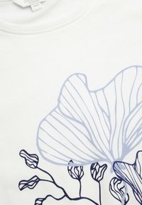 Hvid bomulds t-shirt med en blå blomsterlinjetegning, der har detaljerede konturer og varierende tykkelser, hvilket fremhæver et moderne grafisk design.