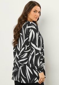 Langärmlige Bluse mit lockerer Passform, mit schwarzem Hintergrund und weißem Blattmuster, aus leichtem Stoff mit glatter Textur.