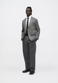 Hall hall ülikond peene mustriga, valge särk, must lips ja mustad kingad. Kohandatud istuvusega ühekordse nööpimisega jakk ja sirge lõikega püksid.