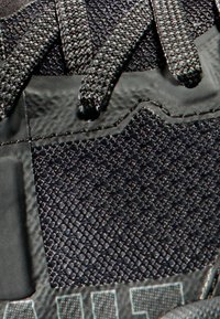 Schwarzer Sportschuh mit strukturiertem Material, kontrastierenden Schnürsenkeln und Gummi-Akzenten. Auffällige Nahtdetails entlang der Nähte.