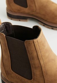 Botines de ante marrón con paneles laterales elásticos y tejido texturizado contrastante. Detalles de costura y una suela resistente.