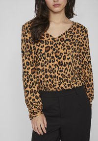 Bluză cu imprimeu de leopard în nuanțe de portocaliu și negru, cu decolteu în V, mâneci lungi și un material moale și ușor. Purtați cu pantaloni negri.