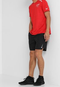 Camiseta roja de Nike de manga corta con diseño texturizado, pantalones cortos negros de Nike y zapatillas deportivas negras con acentos blancos.