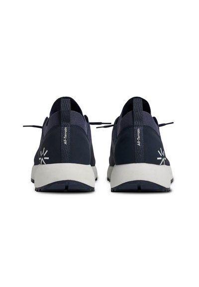 Paire de baskets tout-terrain noir et blanc vues de dos, avec des languettes et des logos réfléchissants sur le talon.