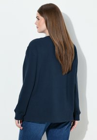 Sudadera oversize azul marino con mangas largas, escote redondo y puños acanalados, combinada con vaqueros de denim. Diseño sencillo y casual.