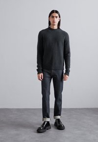 Pull gris foncé avec un col rond, associé à un jean en denim foncé retroussé aux poignets et des chaussures noires à lacets. Design simple, tissu texturé.