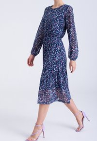 Kukallinen mekko, jossa on tummansininen pohja, pitkät puffihihat, joustava vyötärö ja polvipituus; siinä on vaaleanpunaisia ja valkoisia kukkia. Yhdistetty laventelinvärisiin korkokenkiin.