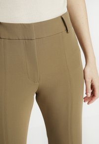 Pantalon kaki à coupe ajustée, avec une texture lisse, des poches latérales et une taille avec passants de ceinture.