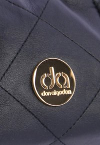 Cuero acolchado azul marino con un logotipo circular dorado grabado con "don algoden." Un patrón de costura prominente realza la textura.