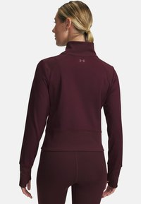 Bordeauxroter Sportjacke mit hohem Kragen und Daumenlöchern. Glattes Material, figurbetontes Design und dezentes Logo auf der Rückseite.