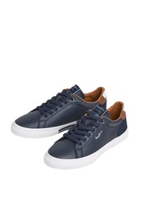 Tengerészkék bőr felsőrészű tornacipők, fehér gumi talppal, barna díszítéssel a saroknál és fekete fűzőkkel. A nyelvén márkajelzés található.