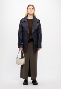 Veste en denim oversize avec grand col, pull marron, jupe longue marron avec fente, portant un sac à main beige et des bottes à plateforme noires.