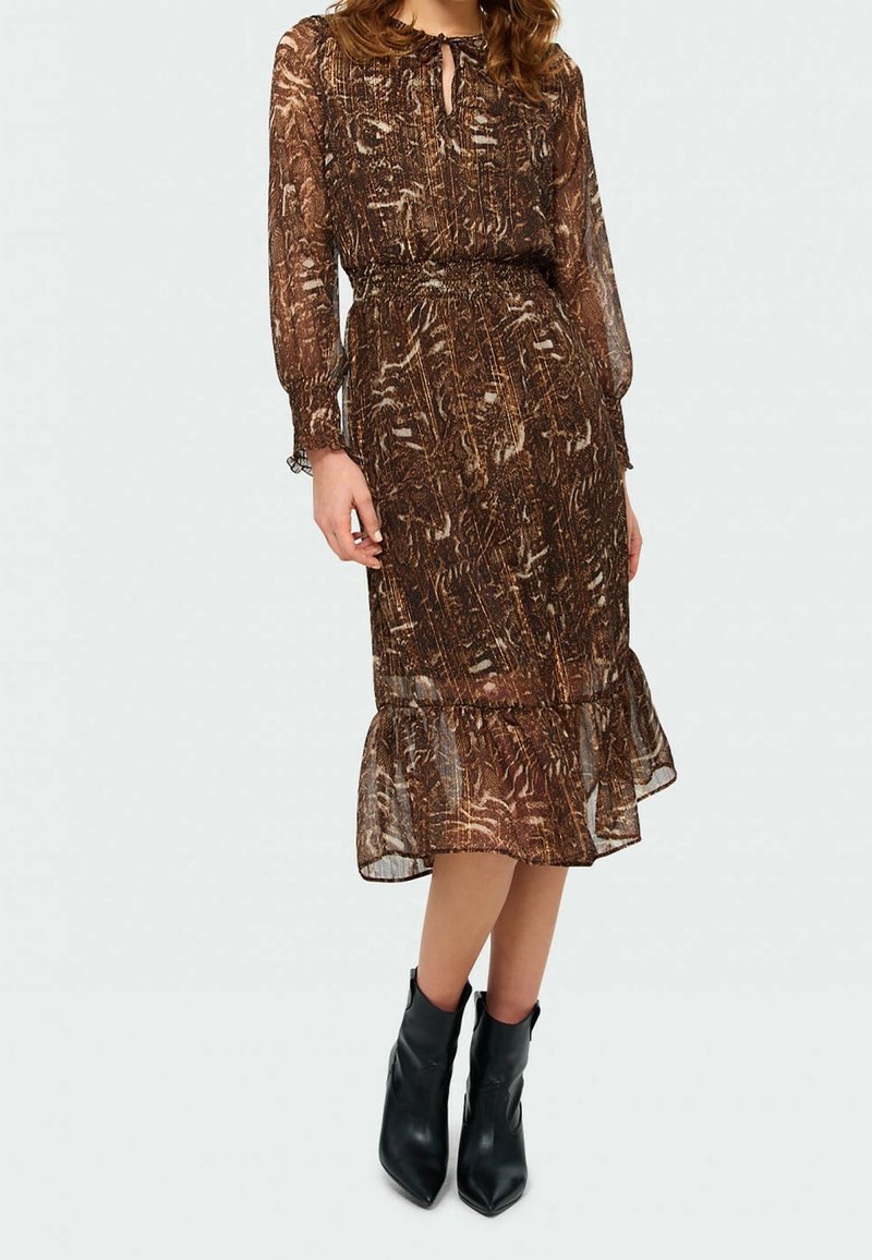 Brun mönstrad klänning med knytkrage, långa ärmar och volangfåll, matchad med svarta ankelstövlar. Halvgenomskinligt tyg.