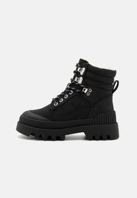 Botas negras hasta el tobillo con un collar acolchado, herrajes plateados, paneles de gamuza texturizada y una suela de goma gruesa con un patrón de relieve profundo.