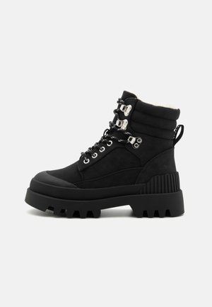 Botas negras hasta el tobillo con un collar acolchado, herrajes plateados, paneles de gamuza texturizada y una suela de goma gruesa con un patrón de relieve profundo.