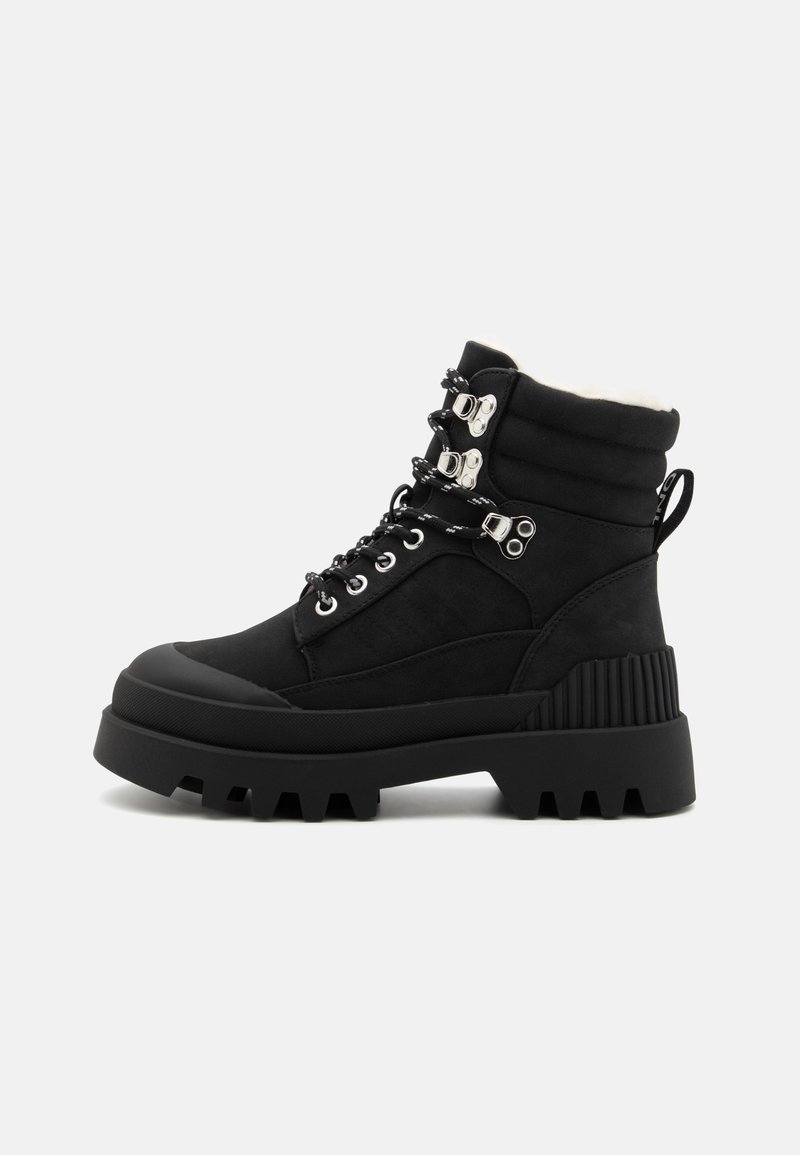 Botas negras hasta el tobillo con un collar acolchado, herrajes plateados, paneles de gamuza texturizada y una suela de goma gruesa con un patrón de relieve profundo.