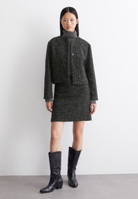 Schwarzes Tweed-Jackett und Rockset mit texturiertem Finish; verfügt über einen hohen Kragen, Knopfverschluss und knielange schwarze Lederstiefel.
