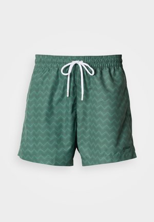 Green swim shorts featuring a chevron pattern, elastic waistband with white drawstring, and a small brand logo on the lower side.