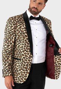 Giacca smoking con stampa leopardata in beige e nero, caratterizzata da un revers in satin nero e un rivestimento interno bordeaux. Vestibilità su misura con tasca frontale.