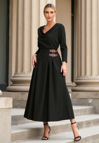 Czarna, długa sukienka z długim rękawem i opadającym dekoltem, z paskiem w talii z brązowymi klamrami oraz zwiewną spódnicą. Czarne sandały na wysokim obcasie.