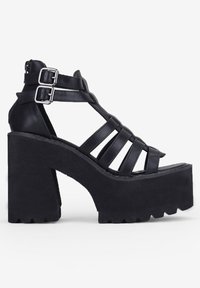 Sandalias negras de tacón alto de cuero con suelas de plataforma gruesas y texturizadas, que cuentan con múltiples correas y doble hebilla para el cierre.