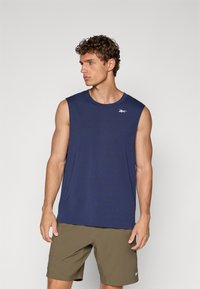 Granatowa bezrękawnik sportowy z okrągłym dekoltem i logo Reebok, w zestawieniu z oliwkowymi szortami, noszony przez modela.