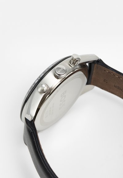 Vue de côté d'une montre-bracelet Hugo Boss en argent avec un bracelet en cuir noir, logo de la marque visible sur la couronne et gravure sur le fond du boîtier indiquant la résistance à l'eau.