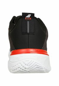 Scarpa sportiva nera con tomaia in tessuto testurizzato, accentuazione rossa sul tallone e suola in gomma bianca con un motivo a scanalature ondulate.