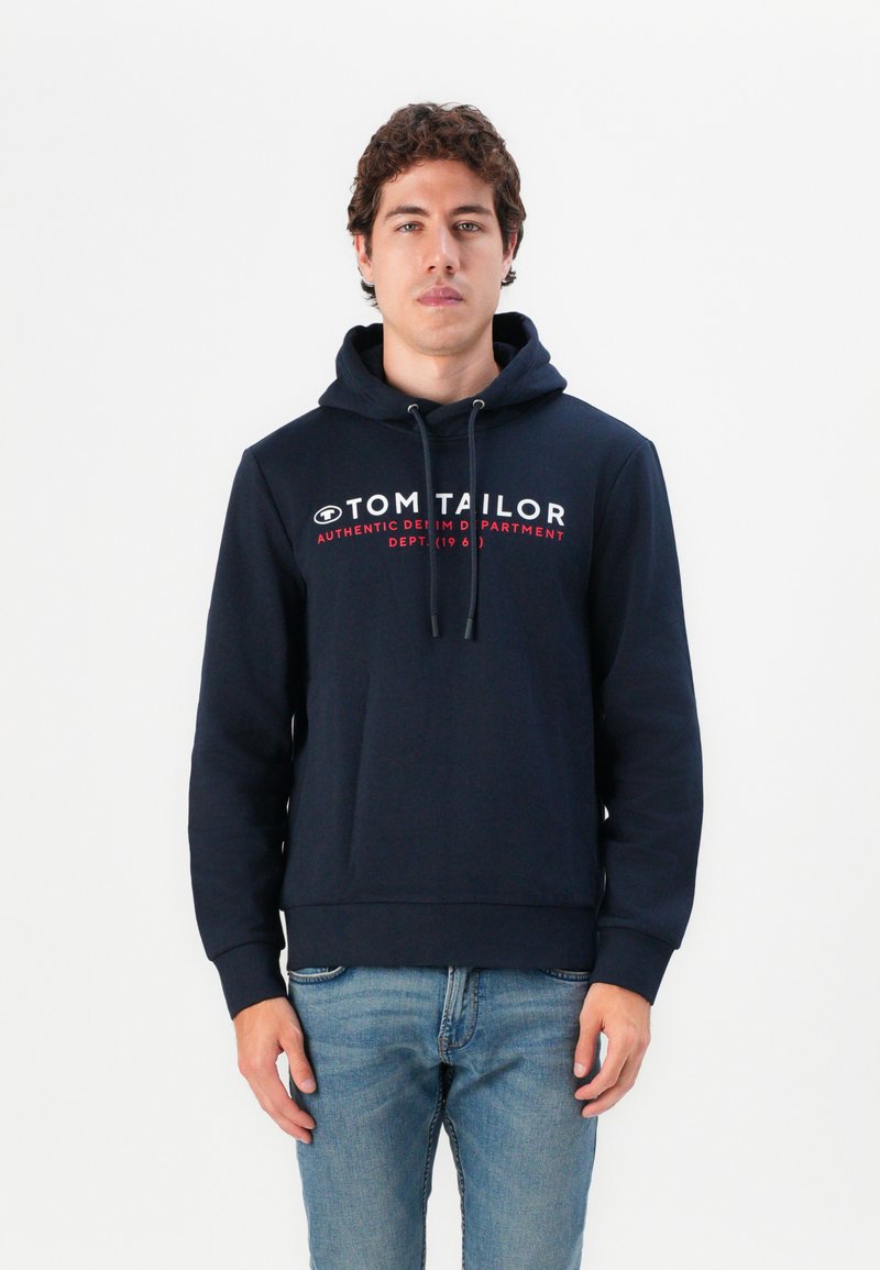 Sudadera con capucha azul marino con cordones, que presenta un destacado texto de logo en blanco y rojo. Tela suave, puños y dobladillo acanalados.