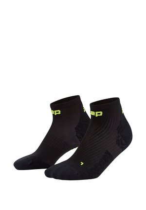 Schwarze Sportsocken mit einem kurzen Knöchelschnitt, ausgestattet mit einem strukturierten Muster und einem leuchtend gelben Logo. Hergestellt aus atmungsaktivem Material.